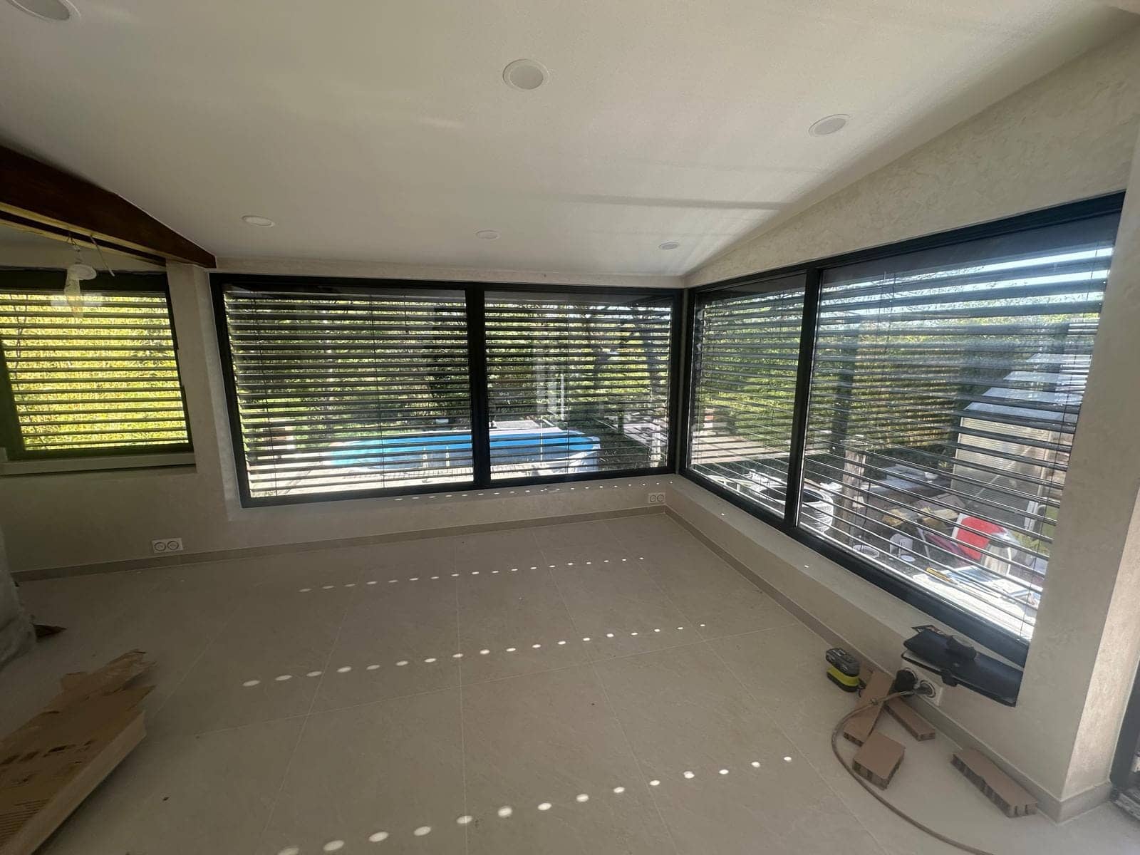 Pièce d'angle avec baies vitrées et brise-soleil orientables donnant sur la piscine, réalisées par REM Fermetures