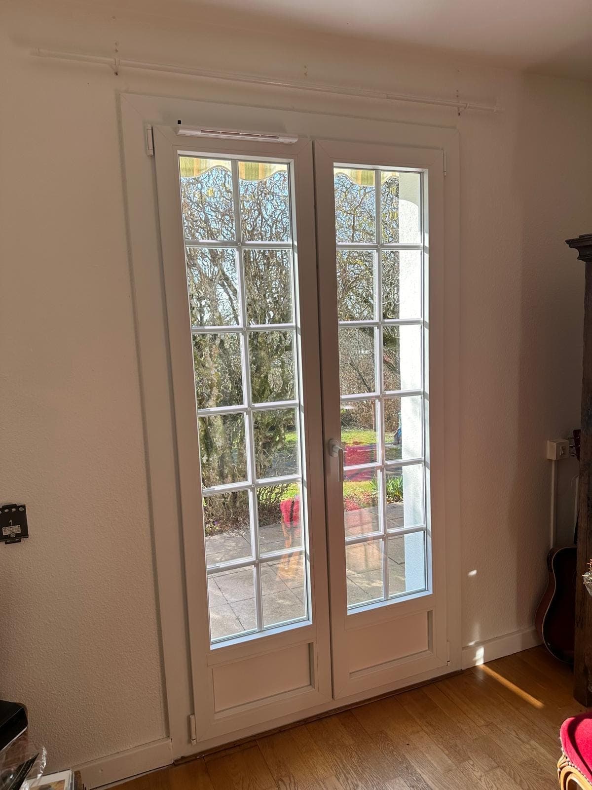 Porte-fenêtre PVC blanche à petits-bois ouvrant sur le jardin, posée par REM Fermetures